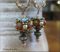 a pair of earrings with beads and stones on them sitting on a table next to a vase