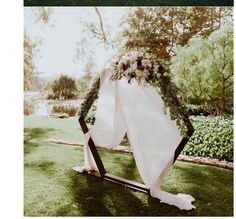 a wedding arch decorated with flowers and greenery on the grass in front of a pond