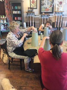 two women sitting at a table making vases with paper machches on top of them