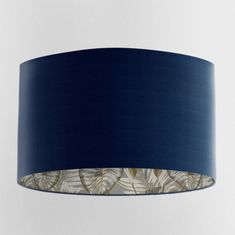 a blue lamp shade hanging from the ceiling with leaves printed on it and a white background