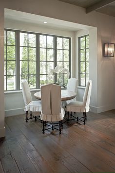 a dinning room table and chairs in front of large windows with wood flooring