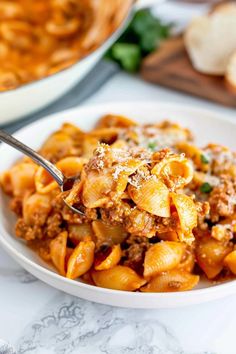 a white bowl filled with pasta and meat on top of a table next to bread