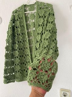 a woman's hand is holding up a green crocheted cardigan