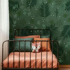 a bed with an orange pillow and green wallpaper