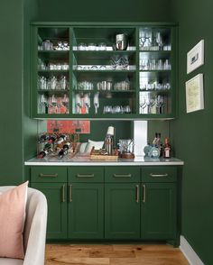 a green cabinet filled with lots of dishes and glasses on top of wooden flooring