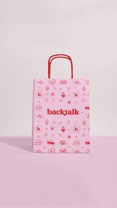 a pink shopping bag with red handles sitting on top of a pink tablecloth covered surface