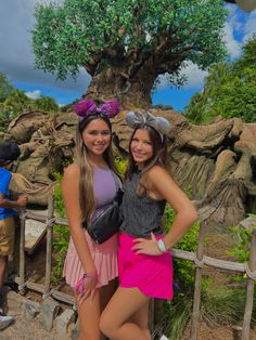 two girls standing next to each other in front of a tree at the animal kingdom