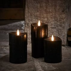 three lit candles sitting next to each other in front of a stone wall and floor