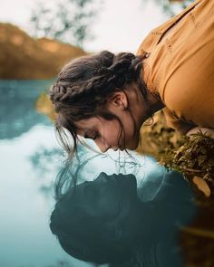 a woman leaning over the edge of a body of water