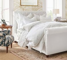 a white bed sitting in a bedroom next to a chair and table with a lamp on top of it