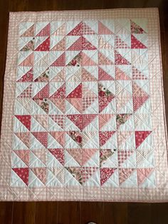 a quilted table runner with pink and red triangles on it, sitting on a wooden floor