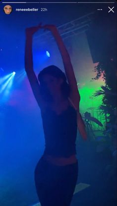 a woman is dancing on stage with her arms in the air and lights behind her