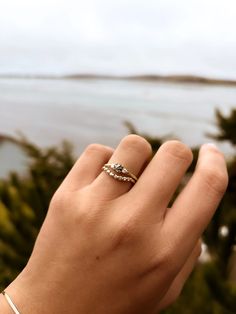 a woman's hand with a ring on top of her finger and the ocean in the background