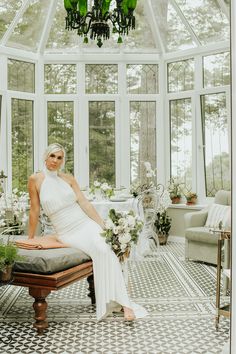 a woman is sitting on a bench in a room with large windows and chandelier