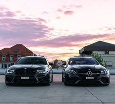 two black cars parked next to each other in front of a pink sky with clouds