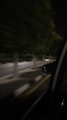 blurry image of cars driving down the road at night time with trees in the background