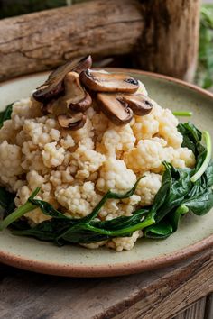 Cauliflower rice topped with sliced mushrooms and surrounded by wilted spinach on a rustic plate.