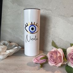 a white coffee cup with an evil eye on it next to pink roses and a vase