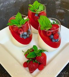 three glasses filled with fruit on top of a white square plate and garnished with green leaves