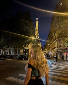 a woman is walking down the street in front of the eiffel tower at night