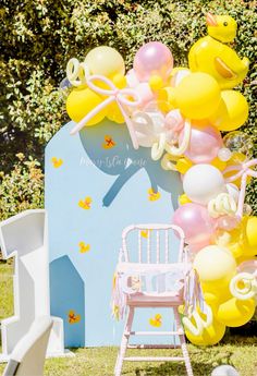 a baby's first birthday party with balloons and decorations on the lawn, including a rocking chair