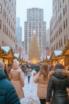 people walking down a snowy street in front of tall buildings with christmas decorations on them