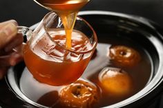 a person pouring syrup into a bowl filled with apples