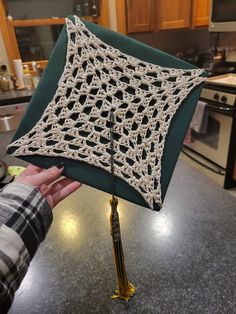 a person holding up a crocheted piece of cloth in a kitchen with wooden cabinets