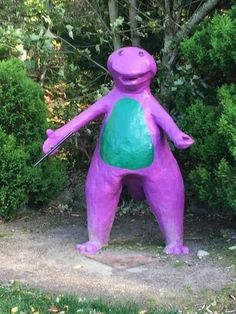 a purple and green dinosaur statue in front of some bushes