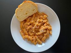 a white plate topped with pasta next to a slice of bread on top of a table