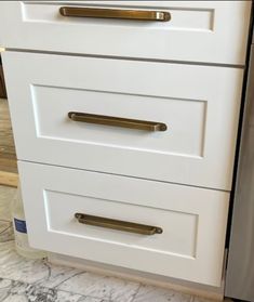 a kitchen with white cabinets and gold pulls on the drawers, in front of a stainless steel dishwasher