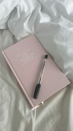 a pink notebook with a pen laying on top of it next to a white sheet