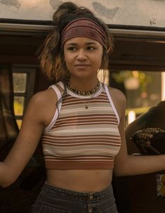 a woman standing in front of a car with her hand on the door handle and wearing a bandana