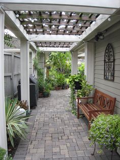 a brick walkway leads to a patio with potted plants on either side and a wooden bench in the middle