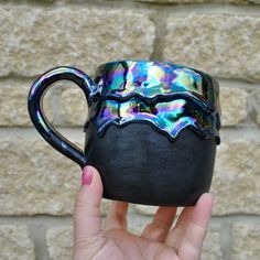 a hand holding a black coffee mug in front of a brick wall