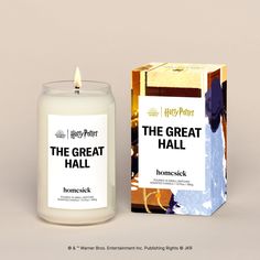 a white candle sitting next to a box on top of a brown table with the words'the great hall'printed on it