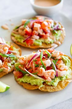 three crackers with shrimp and guacamole on them next to lime wedges