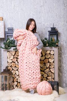 a woman standing in front of a fire place holding a large pink knitted blanket