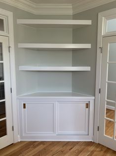 empty white shelves in the corner of a room with wood flooring and glass doors