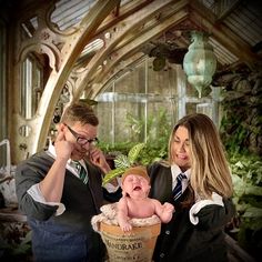 a man and woman standing next to a baby in a bucket with plants on it