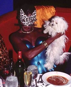 a woman sitting at a table with a dog in her lap and some wine glasses