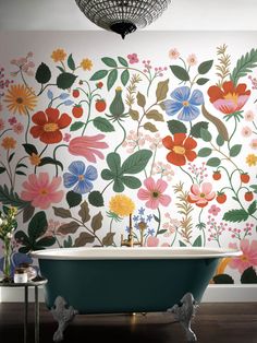 a bath tub sitting under a chandelier next to a wall with flowers on it