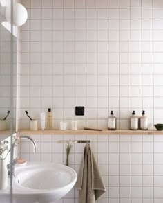 a bathroom with white tiled walls and flooring next to a sink, mirror and towel rack