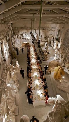 an aerial view of a long table in a room filled with white statues and people