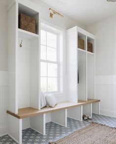 a white room with a bench and some baskets on the shelf next to it's windows