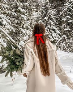 a woman with long hair wearing a white coat carrying a christmas tree in the snow