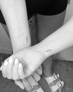 two people holding hands with tattoos on their arms and one has a lightning tattoo on the wrist