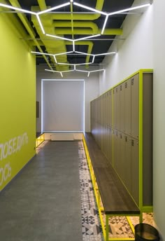 an empty hallway with yellow lockers and black ceiling tiles on the walls, in front of a green wall