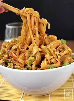 someone is holding chopsticks over noodles in a white bowl on a yellow place mat