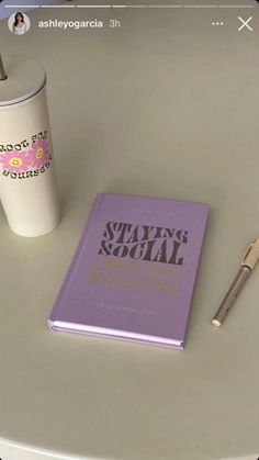 a book, pen and cup sitting on a table next to a coffee cup with a straw in it